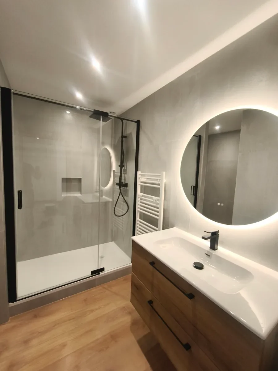 Salle de bain avec douche vitrée, vasque et miroir rond